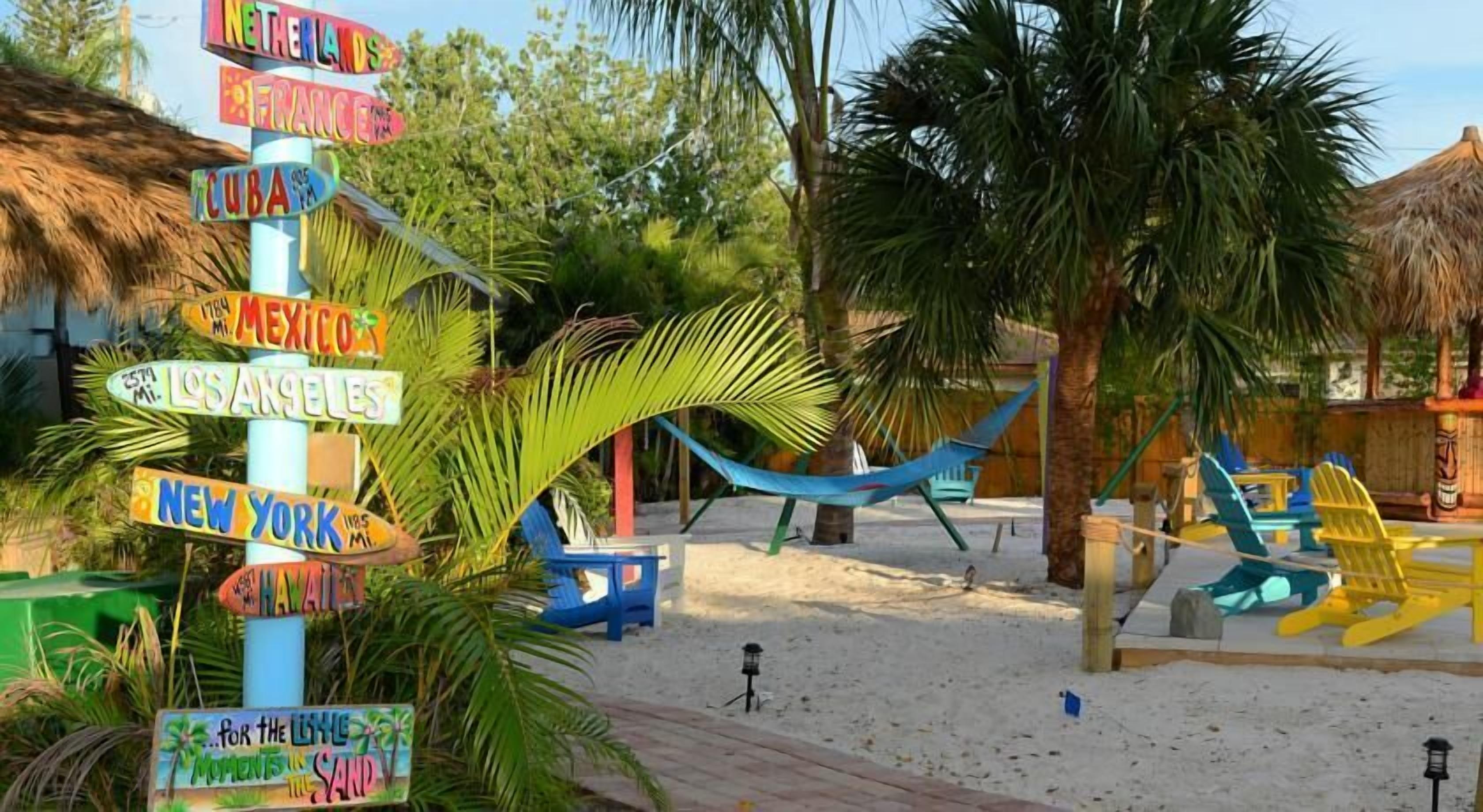 Une zone de plage avec un panneau indiquant différentes destinations, un hamac et des chaises de plage.