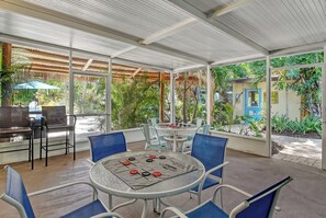 A covered outdoor seating area with tables and chairs, surrounded by lush greenery and a thatched roof structure. - Siesta Key Palms Hotel - Key Suite (Sarasota)