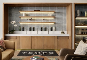 A modern kitchen with wooden cabinets, a marble countertop, and a backsplash of gray tiles. There are shelves with kitchenware and a potted plant.