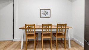 Et spiseområde med et træbord og stole, et billede i ramme på væggen, og en dør til venstre.