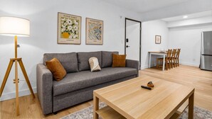En moderne stue med en grå sofa, et træbord og et spiseområde med et lille bord og stole.