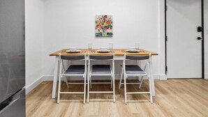 Un petit coin repas avec une table en bois et quatre chaises, une porte blanche et une œuvre d’art colorée accrochée au mur.