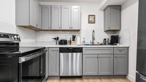 Une cuisine moderne avec des meubles gris, un lave-vaisselle en acier inoxydable, une cuisinière noire et un réfrigérateur noir.
