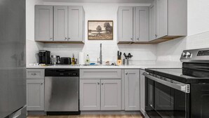A modern kitchen with grey cabinets, a dishwasher, a stove, and a sink. - Designer Loft in Pueblo – Central Modern Comfort (Pueblo)