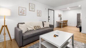 A modern living room with a grey sofa, white coffee table, and a floor lamp. There is a dining area with a table and chairs, and a kitchen with a refrigerator. - Designer Loft in Pueblo – Central Modern Comfort (Pueblo)