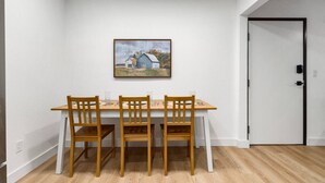 Un comedor con una mesa blanca y sillas de madera, un cuadro enmarcado sobre la mesa, y una puerta a la derecha.