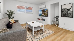 Una sala de estar moderna con un sofá gris, una mesa de centro blanca, un televisor y un cuadro enmarcado en la pared.