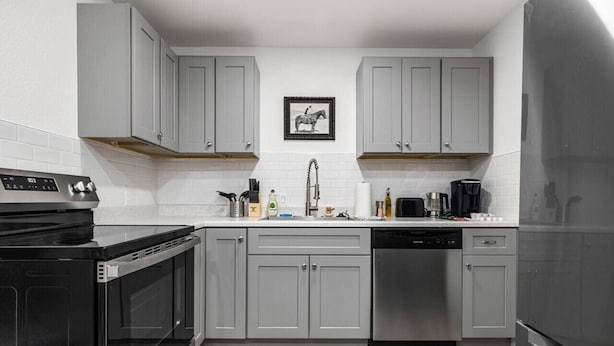 Una cocina moderna con gabinetes grises, una estufa negra y un refrigerador de acero inoxidable.