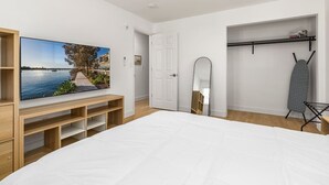 Un dormitorio con una cama grande, un televisor sobre un mueble de madera, un armario, un espejo y un tendedero.