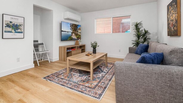 A modern living room with a grey sofa, a wooden coffee table, and a patterned rug. There is a TV mounted on the wall, a plant, and a framed picture. - NEW ! Stylish Loft in DT Pueblo – Sleeps up to 6 (Pueblo)