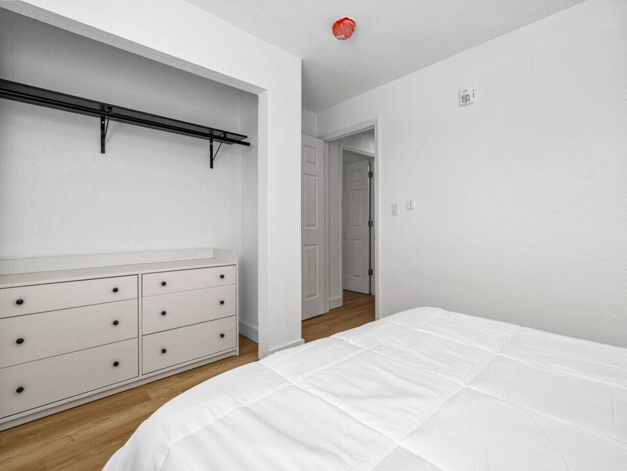 Un dormitorio con cama, cómoda y armario con barra para colgar.