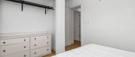 Un dormitorio con cama, cómoda y armario con barra para colgar.