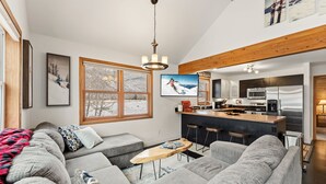 A modern living room with a large gray sectional sofa, a wooden coffee table, and a TV mounted on the wall. A kitchen with a bar area is visible in the background. - 3B/2BA + Loft | Eagle-Vail• Dog-Friendly (Avon)