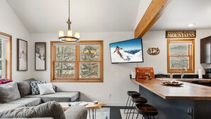 A modern kitchen with a bar area, large windows, and a television displaying a skier. - 3B/2BA + Loft | Eagle-Vail• Dog-Friendly (Avon)