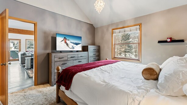 A bedroom with a bed, a television, a dresser, a window with a view, and a chandelier. - 3B/2BA + Loft | Eagle-Vail• Dog-Friendly (Avon)