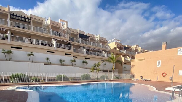 A swimming pool with a clear blue water, surrounded by a tiled deck and a white railing. - Modern Apartment with Large Flower Terrace & Pool – Chayofa, Tenerife (Chayofa)
