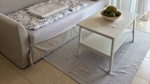 A minimalist living room with a sofa, a coffee table, and a window with sheer curtains. - Modern Apartment with Large Flower Terrace & Pool – Chayofa, Tenerife (Chayofa)