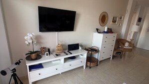 A living room with a flat-screen TV, white furniture, a telescope, and a fruit bowl. - Modern Apartment with Large Flower Terrace & Pool – Chayofa, Tenerife (Chayofa)