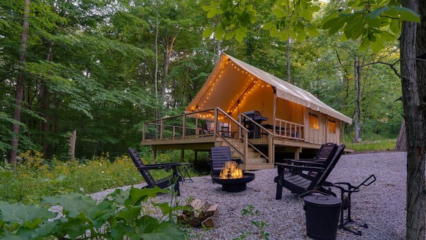 A tent-style accommodation with a deck, outdoor seating, and a fire pit.