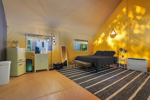 Quarto compacto com cama, mesa de cabeceira, luminária e vista para o exterior.