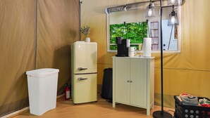 A compact room with a white refrigerator, a small cabinet, a black suitcase, and a floor lamp.