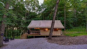 A cabin with a deck, surrounded by trees, and a gravel ground.