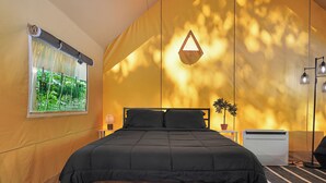 A bedroom with a bed, a window with a view, a bedside table, and a wall-mounted lamp.