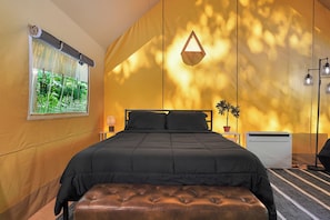 Un dormitorio con cama, ventana con vistas, mesita de noche y lámpara de pared.