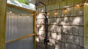 A shower with a wooden shingled wall, a metal door, and string lights.
