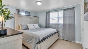 Ein Schlafzimmer mit einem Bett, einem Nachttisch, einer Topfpflanze und einem Fenster mit Vorhängen.