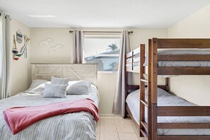A bedroom with a bunk bed, a single bed with striped bedding, and a window with curtains. - Private Heated Pool + Grill | Cozy Coastal (Sarasota)