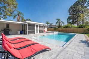 Une piscine avec des chaises longues, un patio couvert et une clôture en bois.