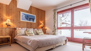 Ein gemütliches Schlafzimmer mit Holzwand, einem großen Fenster und einem Bett mit floralem Bettzeug.