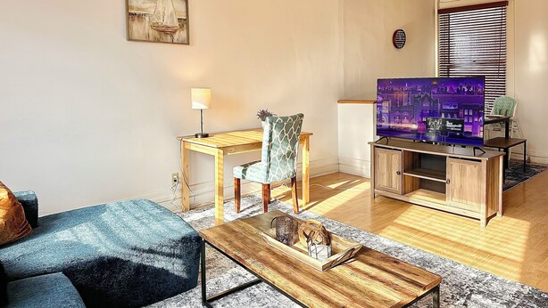 Ein Wohnzimmer mit einer Couch, einem Couchtisch, einer TV-Bank mit Flachbildfernseher, einer Lampe und einem Sessel.