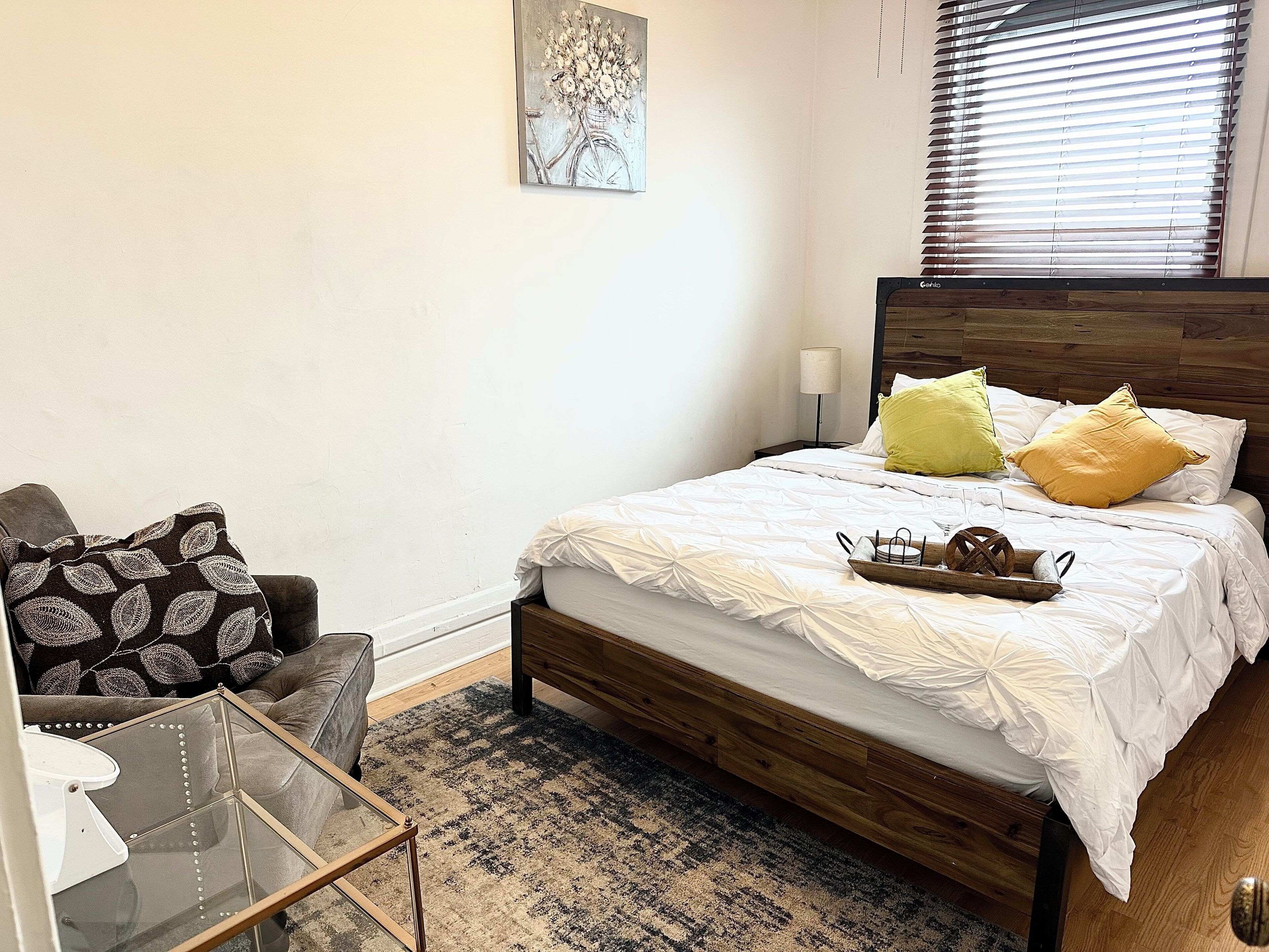 Ein Schlafzimmer mit einem hölzernen Bett, einem Glastisch, einer Couch und einem Kissen mit Muster.