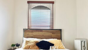 Ein ordentlich bezogenes Bett mit Holz Kopfteil, weißer Bettwäsche und dekorativen Kissen.
