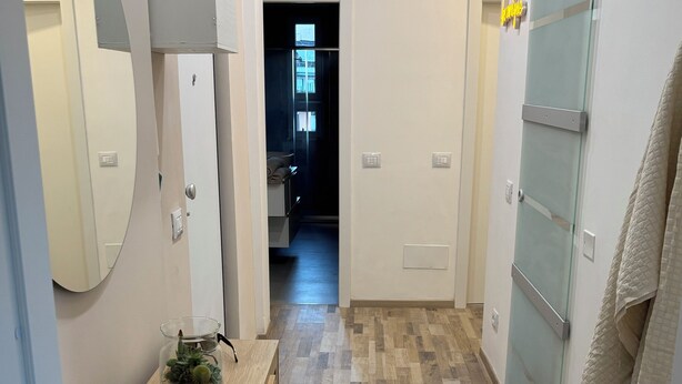 Un couloir doté d’un plancher en bois, une table avec un plateau en verre sur laquelle se trouve une plante, un miroir et une serviette accrochée à une porte.