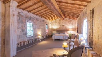 A rustic room with exposed wooden beams, a bed, a desk with a lamp, and bookshelves.