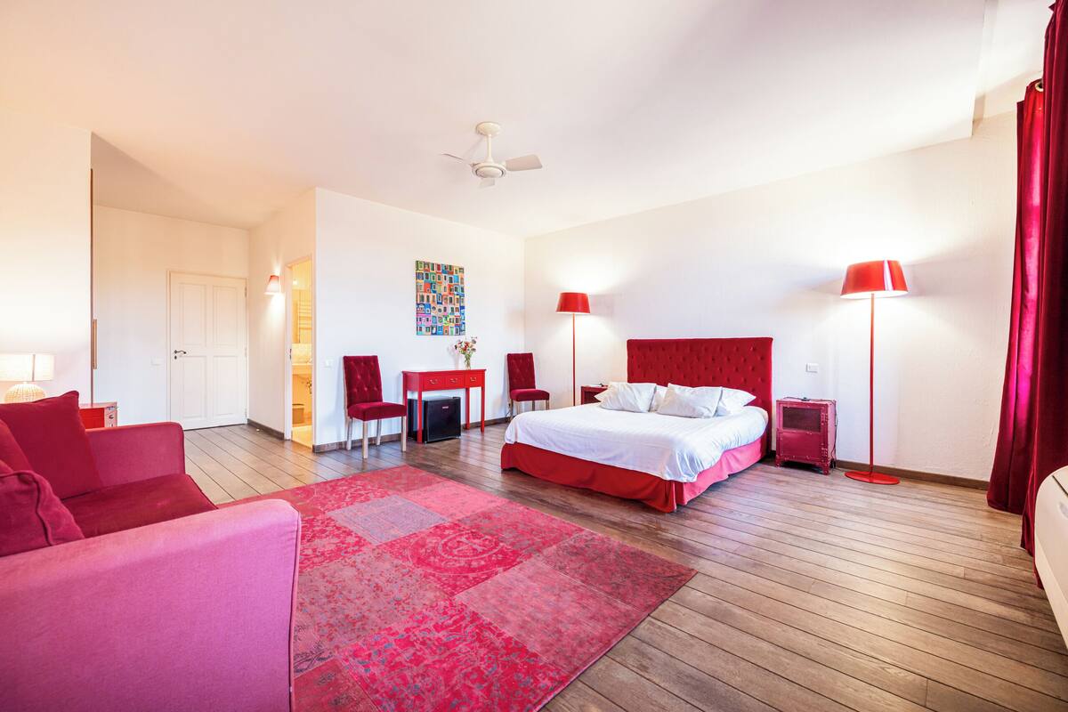 Een hotelkamer met een bed, een bureau, een stoel, een rode bank en een rood vloerkleed.