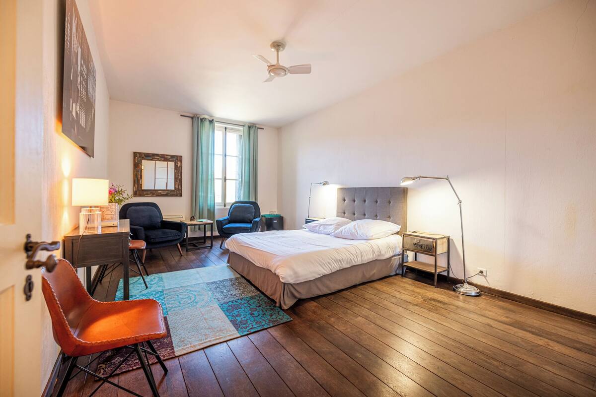 Een hotelkamer met een bed, bureau, stoel en een plafondventilator.