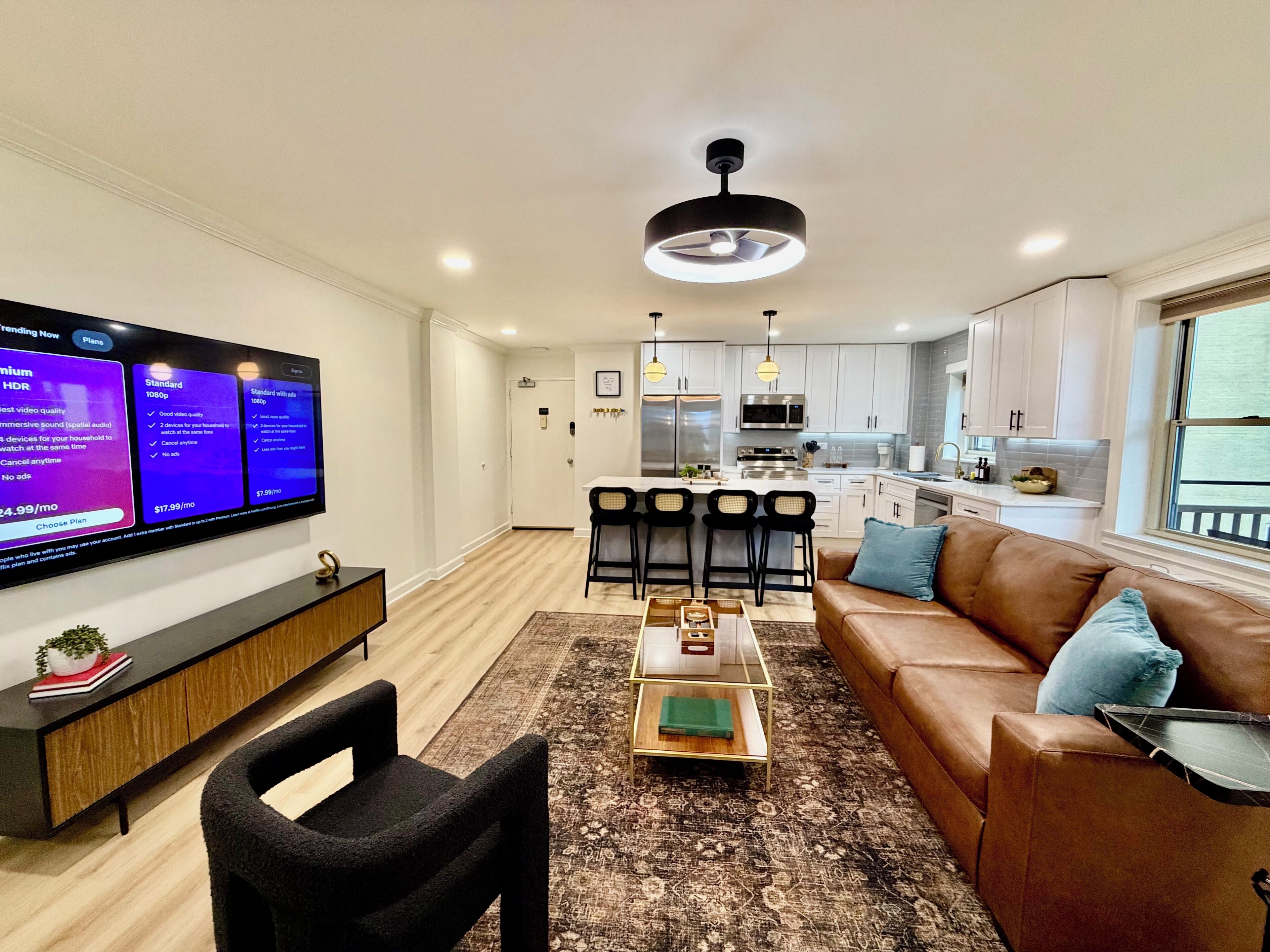 A modern living room with a flat-screen TV, a brown leather sofa, a coffee table, and a patterned rug.
