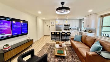 A modern living room with a flat-screen TV, a brown leather sofa, a coffee table, and a patterned rug.