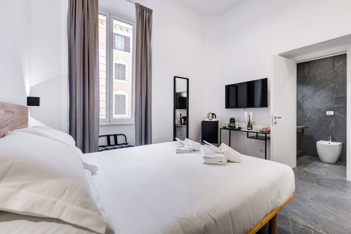 Une chambre d’hôtel dotée d’un grand lit, d’un bureau avec un téléviseur à écran plat, d’un miroir et d’une salle de bain moderne équipée d’un bidet.