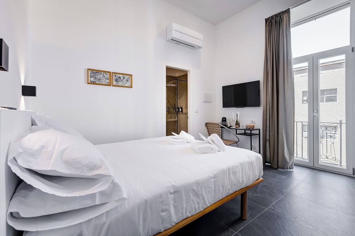 Une chambre d’hôtel avec un lit, une télévision, un bureau et un balcon avec des rideaux.