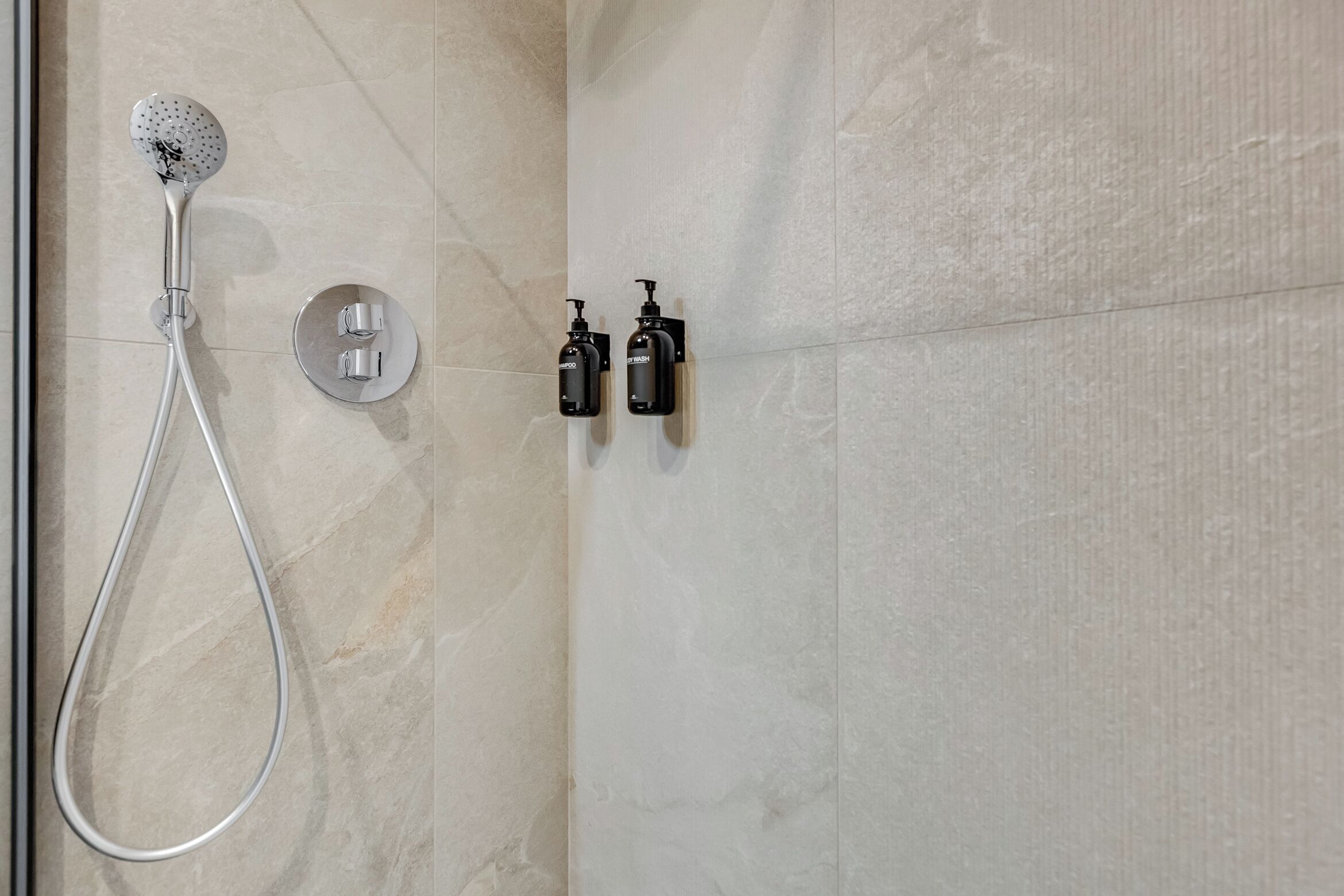 A shower with a handheld showerhead and two bottles of shampoo on the wall.