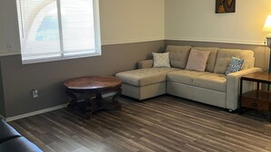 A living room with a sectional sofa, a round wooden table, and a lamp. - Bullhead City Home - Near Colorado River! (Bullhead City)