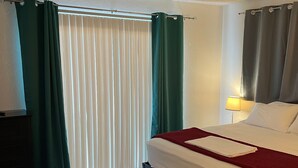 A hotel room with a bed, a nightstand, a lamp, and a window with curtains. - Bullhead City Home - Near Colorado River! (Bullhead City)