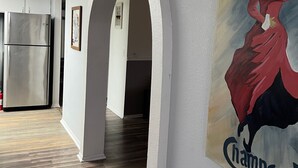 A hallway with a modern kitchen, a refrigerator, and a wooden floor. There is a painting on the wall and an archway leading to another room. - Bullhead City Home - Near Colorado River! (Bullhead City)