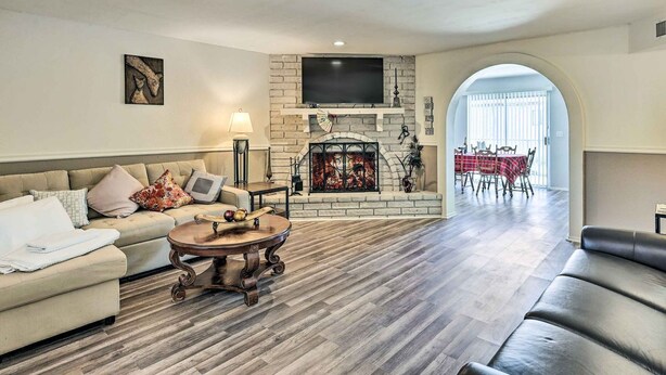A living room with a fireplace, a sofa, a coffee table, and a dining area visible through an archway. - Bullhead City Home - Near Colorado River! (Bullhead City)