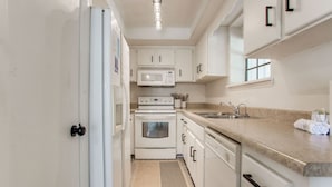 Une cuisine moderne avec des meubles blancs, un four à micro-ondes, un four traditionnel, un évier et un plan de travail.